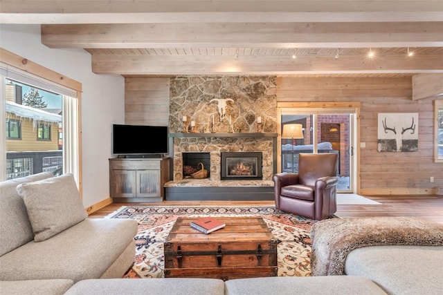 living room featuring light hardwood / wood-style floors, beam ceiling, a stone fireplace, and wooden walls