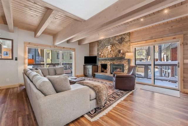 living room featuring hardwood / wood-style flooring, beamed ceiling, a stone fireplace, and wood ceiling