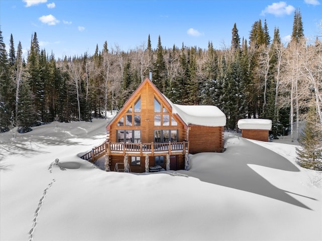 snow covered back of property with a forest view and a deck