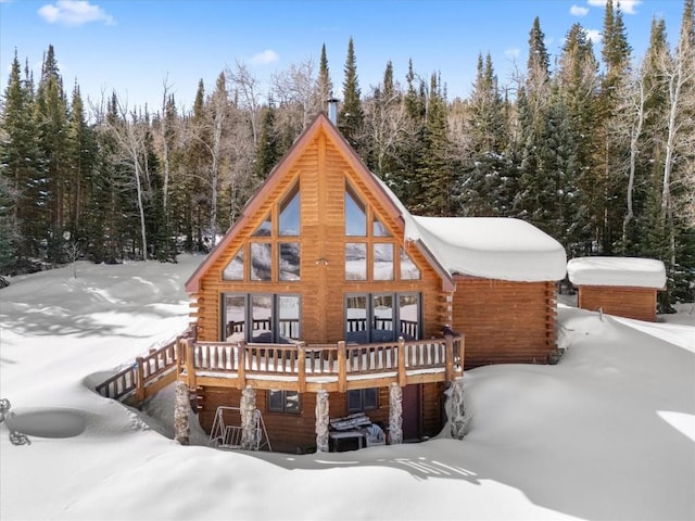 snow covered rear of property featuring log exterior and a forest view