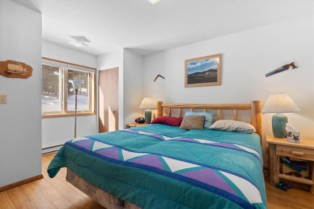 bedroom featuring a baseboard heating unit, wood finished floors, and baseboards