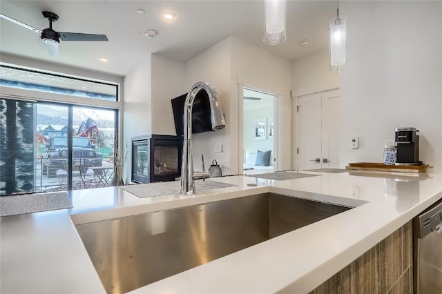 kitchen featuring a multi sided fireplace, sink, stainless steel dishwasher, ceiling fan, and decorative light fixtures