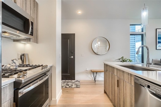 kitchen with pendant lighting, stainless steel appliances, light hardwood / wood-style floors, and sink