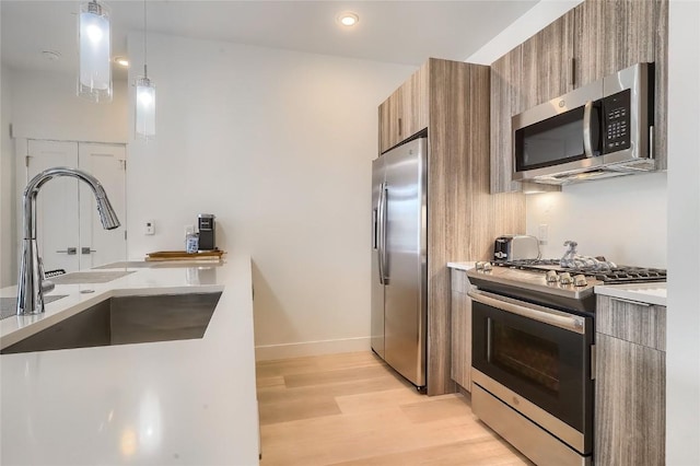 kitchen with pendant lighting, sink, stainless steel appliances, and light hardwood / wood-style flooring