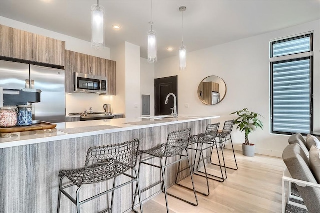 kitchen with kitchen peninsula, a kitchen breakfast bar, stainless steel appliances, pendant lighting, and light hardwood / wood-style flooring