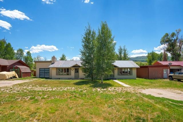 ranch-style home with a chimney, an attached garage, a front yard, metal roof, and driveway