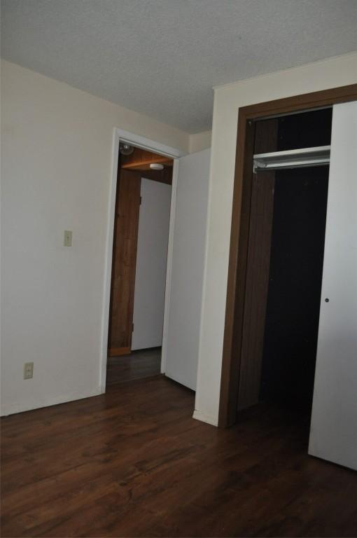 unfurnished bedroom with a textured ceiling, dark wood-style flooring, and a closet