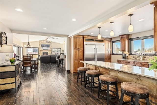 kitchen featuring light stone countertops, backsplash, vaulted ceiling, stainless steel built in fridge, and hanging light fixtures