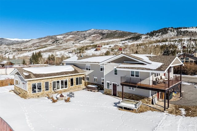 snow covered back of property featuring a jacuzzi and a deck with mountain view