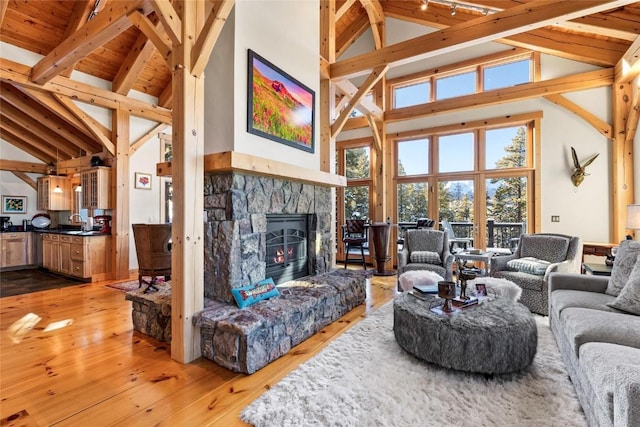 living room featuring light hardwood / wood-style floors, a stone fireplace, sink, high vaulted ceiling, and beamed ceiling