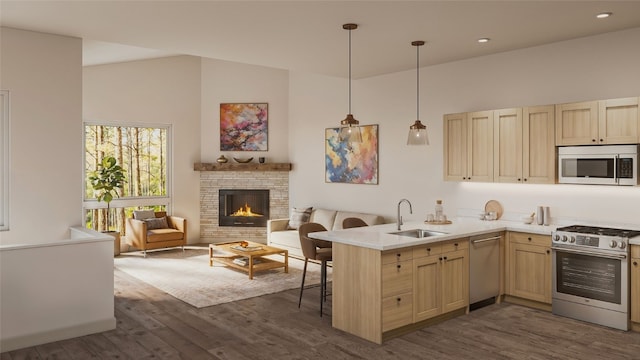 kitchen featuring a kitchen breakfast bar, a stone fireplace, sink, appliances with stainless steel finishes, and kitchen peninsula