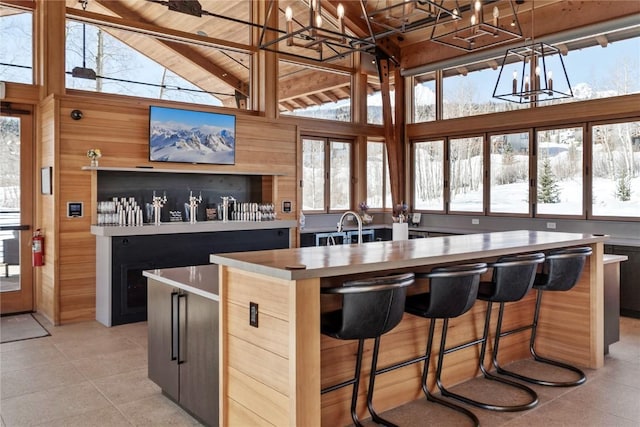 kitchen featuring beamed ceiling, a notable chandelier, a center island with sink, wooden walls, and light countertops