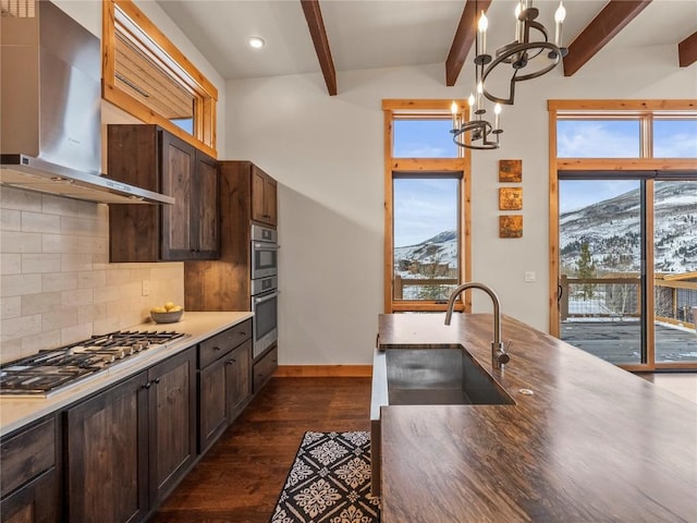 kitchen with a sink, appliances with stainless steel finishes, wall chimney range hood, a notable chandelier, and a mountain view