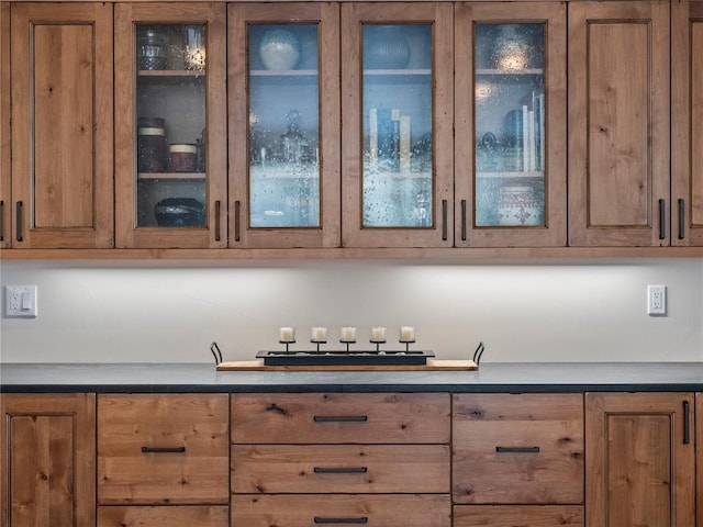 kitchen featuring glass insert cabinets, brown cabinets, and dark countertops