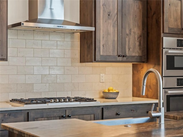 kitchen with tasteful backsplash, stainless steel appliances, wall chimney exhaust hood, light countertops, and dark brown cabinets