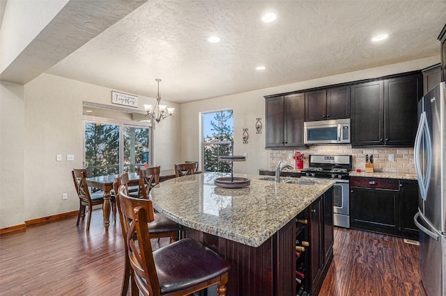 kitchen featuring appliances with stainless steel finishes, sink, hanging light fixtures, light stone counters, and a center island with sink