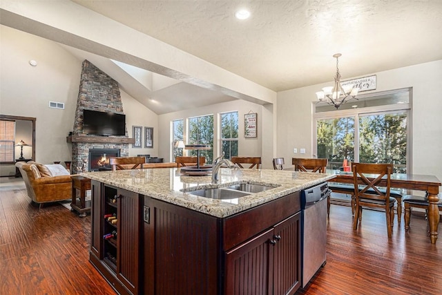 kitchen with sink, light stone counters, dishwasher, a fireplace, and a kitchen island with sink