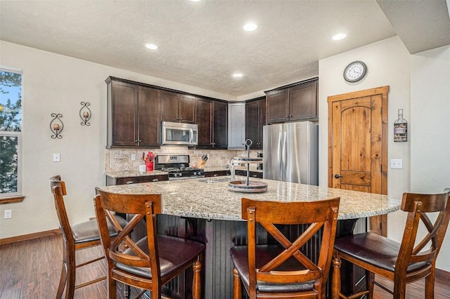 kitchen with stainless steel appliances, a breakfast bar, a kitchen island with sink, and dark brown cabinets