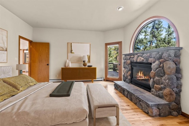 bedroom with access to exterior, light hardwood / wood-style floors, a stone fireplace, and a baseboard heating unit