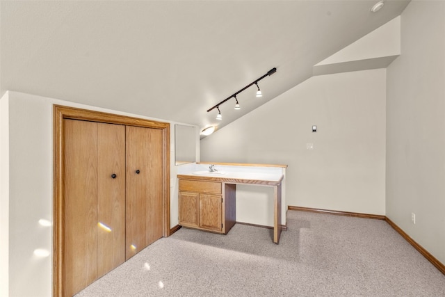 unfurnished bedroom featuring sink, rail lighting, vaulted ceiling, built in desk, and light colored carpet