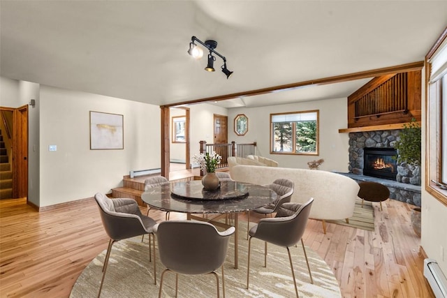 dining room with light wood-type flooring, rail lighting, a stone fireplace, and baseboard heating