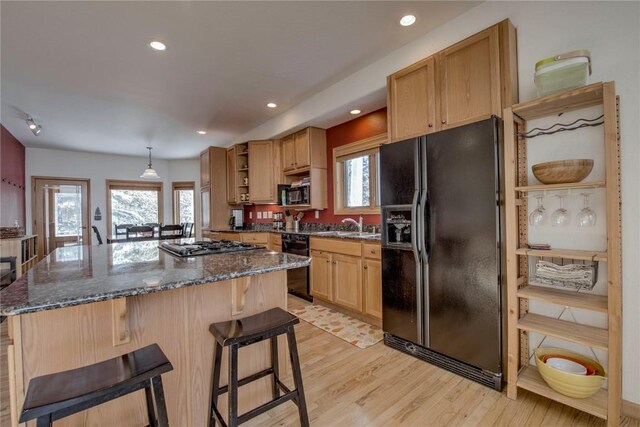 kitchen with dark stone countertops, a breakfast bar, a kitchen island, black appliances, and light wood-type flooring