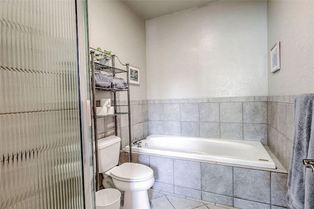 bathroom with tile patterned floors, a relaxing tiled tub, tile walls, and toilet