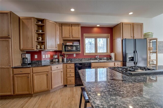 kitchen featuring sink, light hardwood / wood-style floors, dark stone countertops, and black appliances