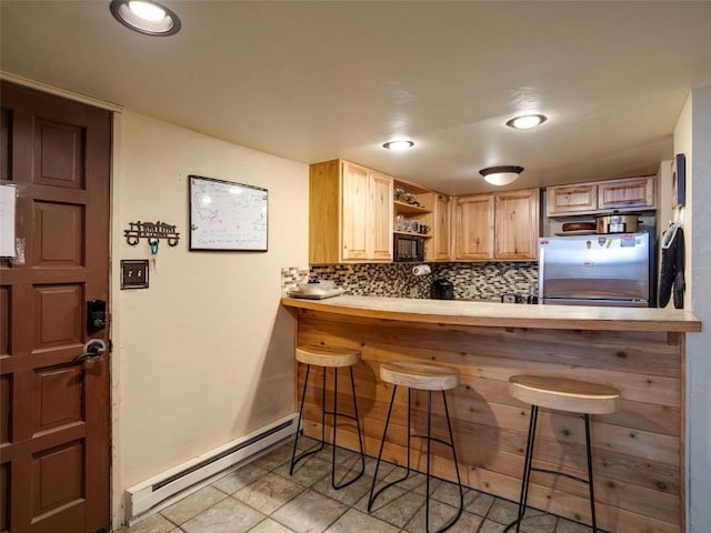 kitchen featuring kitchen peninsula, a kitchen bar, a baseboard heating unit, stainless steel refrigerator, and light brown cabinets