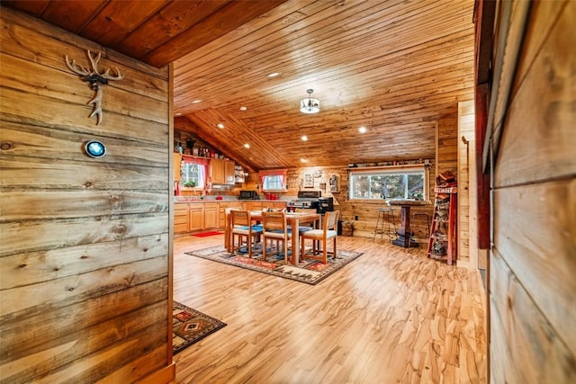 dining space with light wood-type flooring, wooden walls, vaulted ceiling, and wooden ceiling