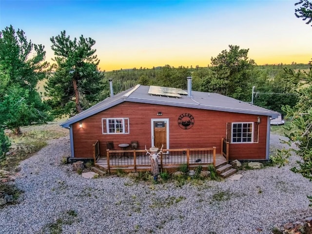 back house at dusk with a wooden deck and solar panels