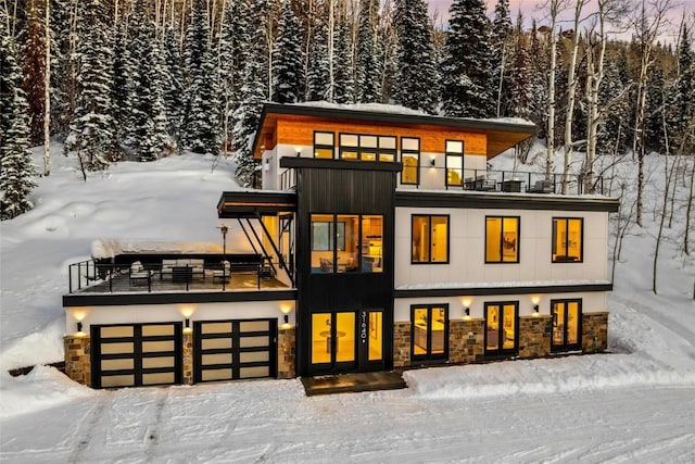 snow covered back of property featuring a balcony and a garage