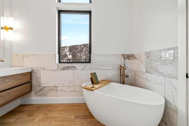 bathroom with tile walls, a tub to relax in, hardwood / wood-style floors, and vanity