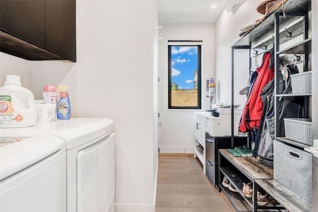 washroom featuring baseboards, washing machine and clothes dryer, cabinet space, and light wood-style floors