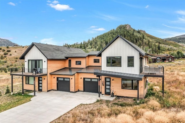 modern farmhouse featuring driveway, metal roof, a mountain view, and a balcony