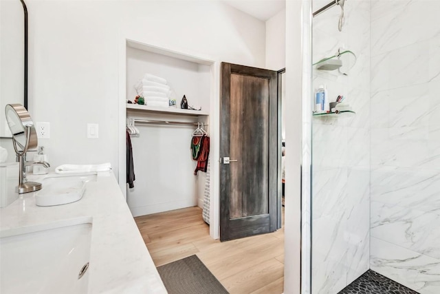 full bath featuring a walk in closet, a marble finish shower, double vanity, a sink, and wood finished floors