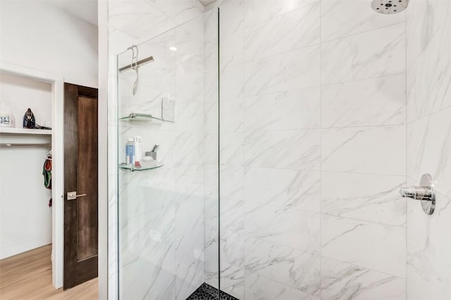 full bathroom featuring wood finished floors, a marble finish shower, and a walk in closet