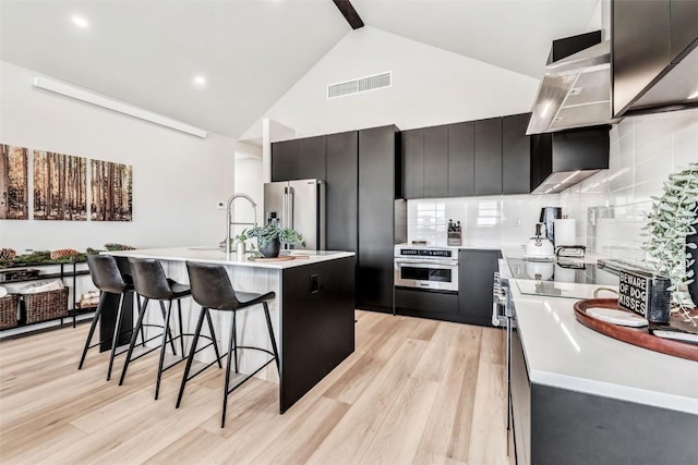 kitchen featuring visible vents, decorative backsplash, a breakfast bar area, dark cabinets, and stainless steel appliances