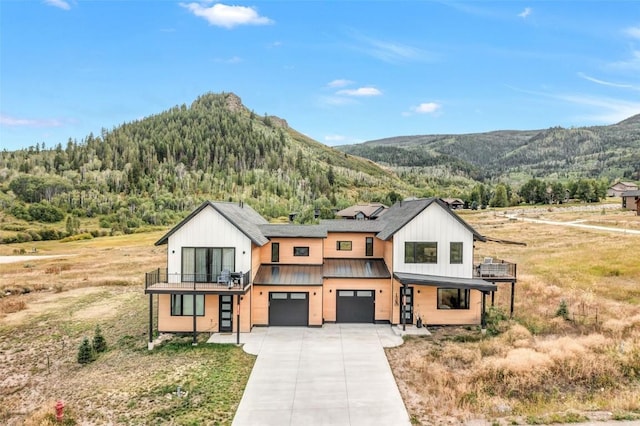 modern farmhouse featuring an attached garage, a mountain view, a balcony, driveway, and a standing seam roof