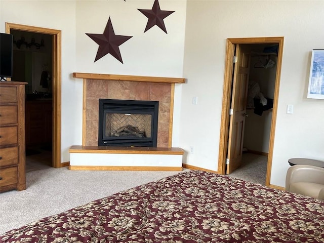 carpeted bedroom with a walk in closet and a tile fireplace