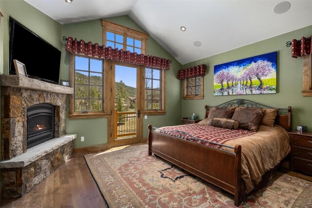 bedroom featuring hardwood / wood-style flooring, a stone fireplace, lofted ceiling, and access to outside