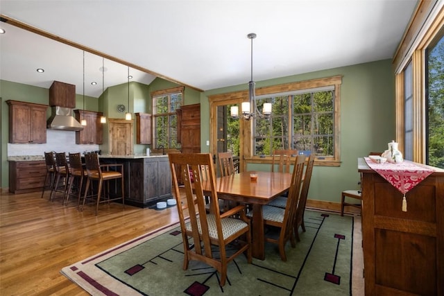 dining room featuring sink, light wood-type flooring, lofted ceiling, and an inviting chandelier