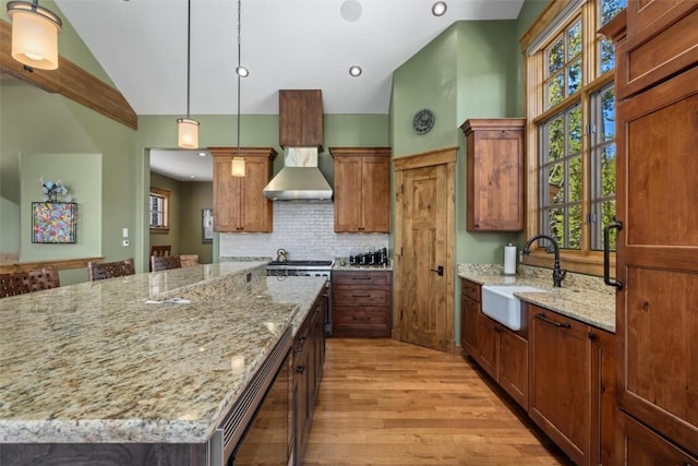 kitchen featuring a large island, sink, wall chimney exhaust hood, light stone countertops, and lofted ceiling