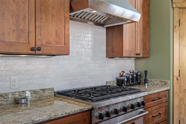 kitchen with high end range, backsplash, light stone counters, and range hood