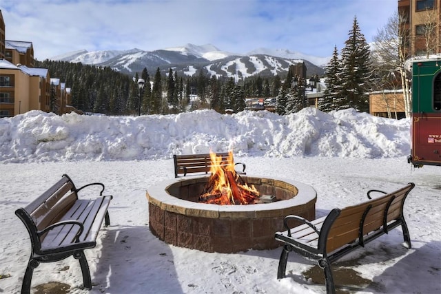 snow covered patio featuring a mountain view and an outdoor fire pit