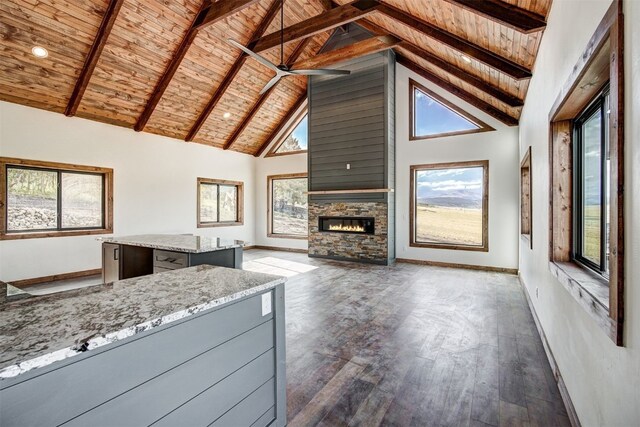 unfurnished living room featuring beam ceiling, wooden ceiling, dark wood-type flooring, a stone fireplace, and high vaulted ceiling