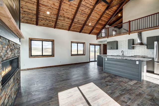 kitchen with backsplash, a tile fireplace, wall chimney range hood, stainless steel fridge, and dark hardwood / wood-style flooring