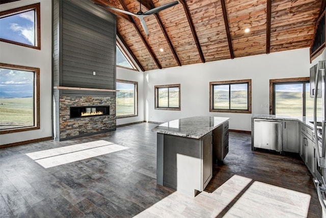 kitchen with a center island, wooden ceiling, a stone fireplace, light stone counters, and high vaulted ceiling