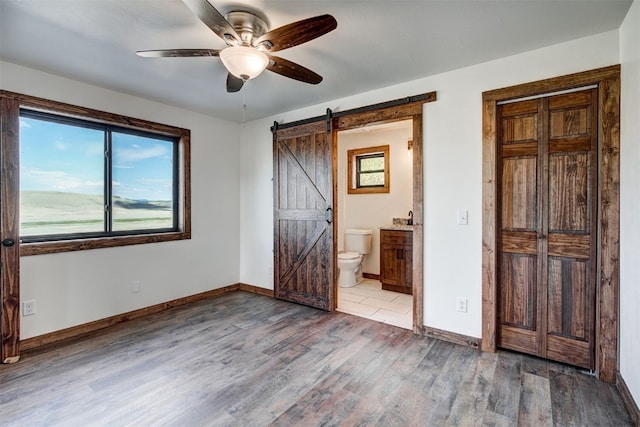 unfurnished bedroom featuring hardwood / wood-style floors, ceiling fan, a barn door, and connected bathroom