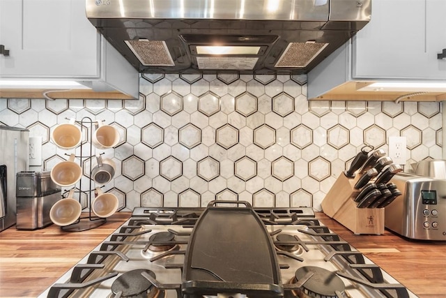 kitchen with decorative backsplash, white cabinetry, and wall chimney range hood